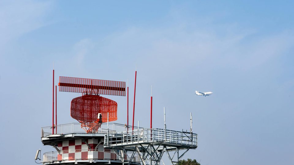 An airport radar tower with an airplane visible in the sky.