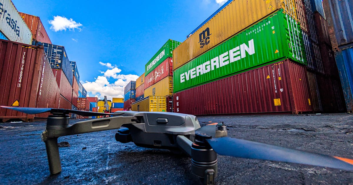 Drone flying above stacked shipping containers in a logistics yard