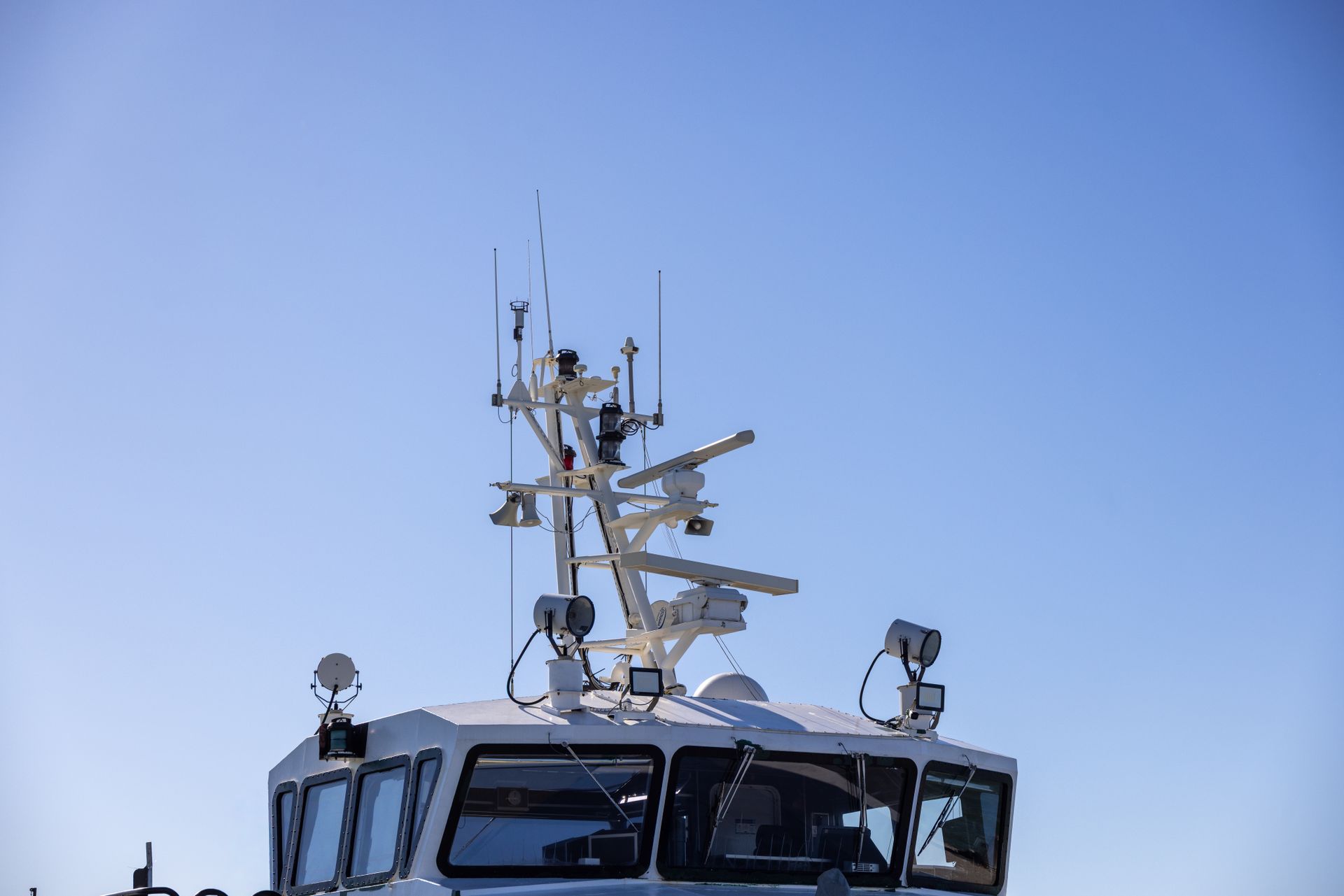Modern radar and communications antennas mounted on a vessel bridge against a clear blue sky