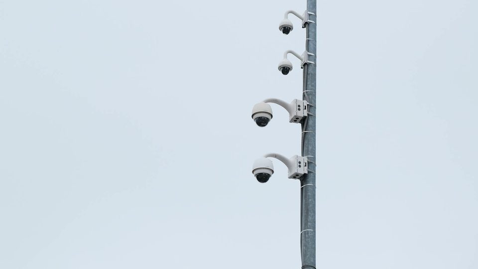 Security cameras mounted together on a metal pole under an overcast sky.