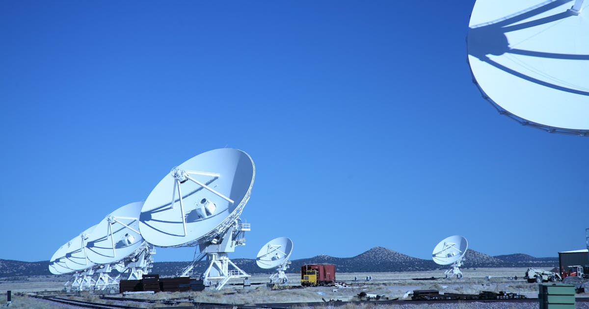 Multiple white satellite dishes aligned in an open field under a blue sky